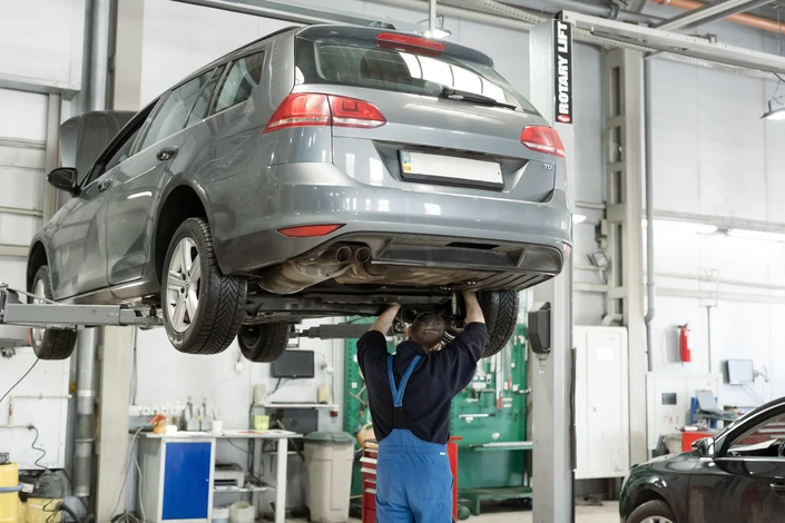 Mécanicien automobile en combinaison bleue travaillant sous le capot ouvert d'une voiture rouge dans un garage professionnel