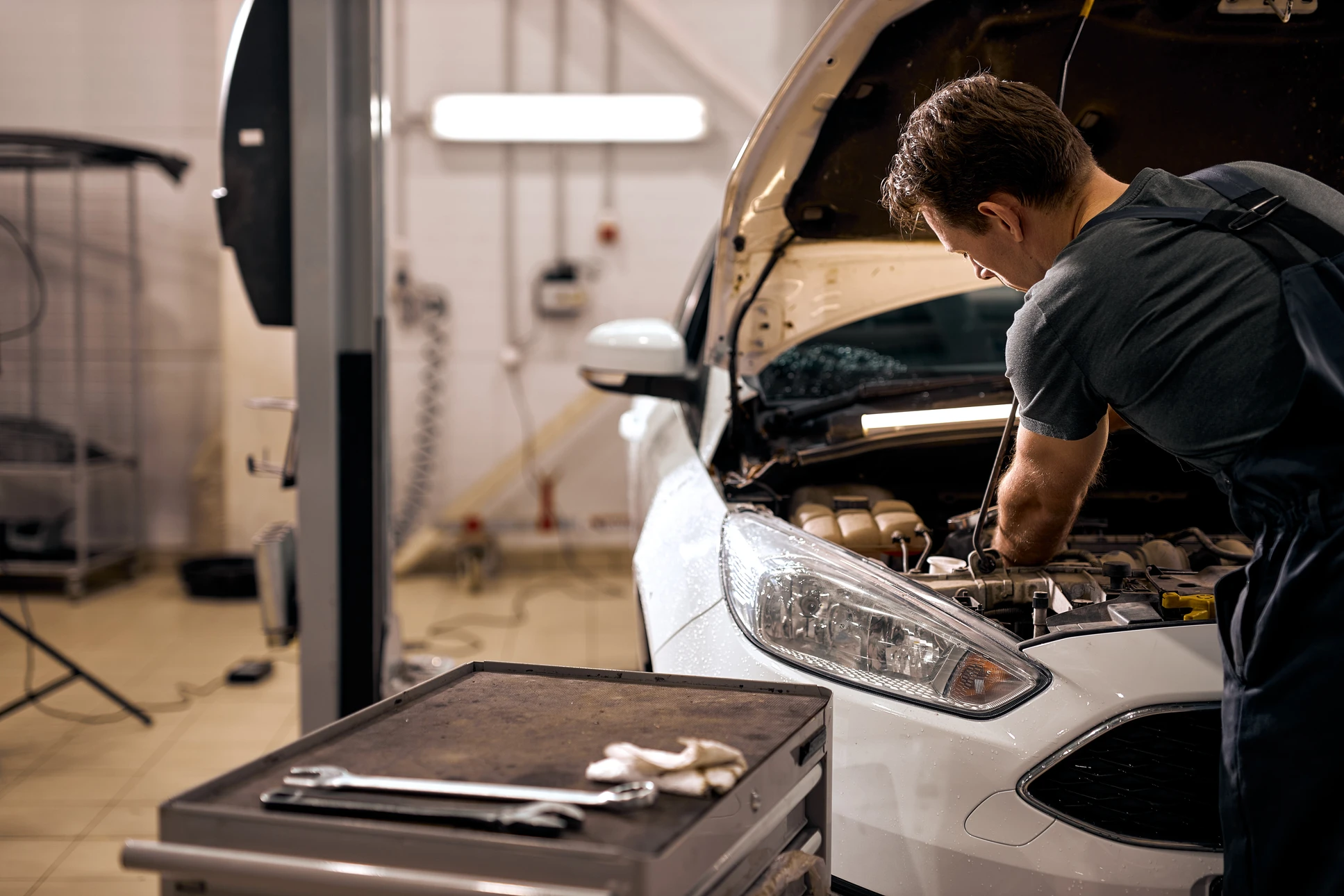 Mécanicien automobile en combinaison bleue et casquette travaillant sur une voiture de sport noire décapotable dans un garage professionnel