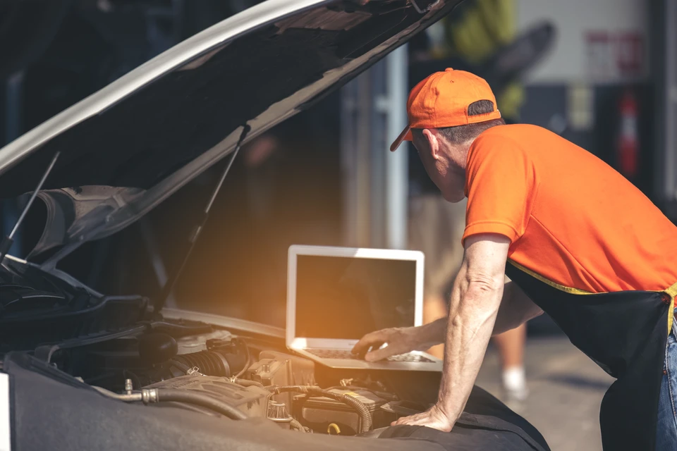 Garage automobile avec technicien en combinaison rouge effectuant maintenance sur véhicule